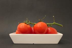 red tomatoes on a branch in a white bowl