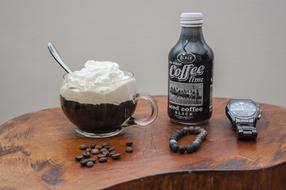 Beautiful coffee cup and bottle, coffee beans, necklace and watch on the wooden table