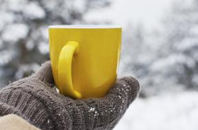 Yellow Cup on hand in glove at snowy winter