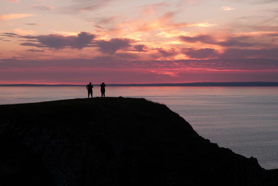 silhouettes of people on a hill against a pink evening sky