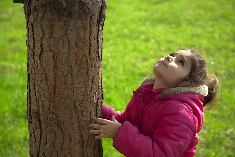 a girl in a pink jacket stands by a tree