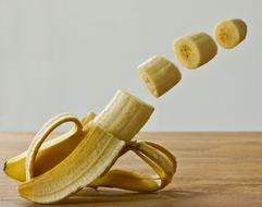 Beautiful, yellow banana with the cut pieces, in movement, above the wooden surface