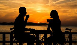 silhouette of a couple drinking coffee on the background of golden sunset