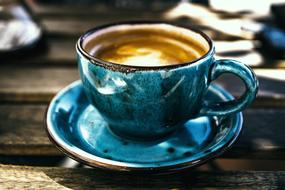 Beautiful blue cup in the different shades, with the brown and white coffee, on the wooden table