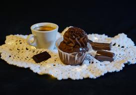 Beautiful chocolate cupcake and pieces, near the cup of coffee, on the beautiful, white, patterned napkin, at black background