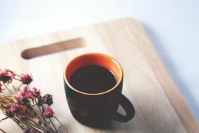 Coffee in dark cup and dry flowers on wooden board