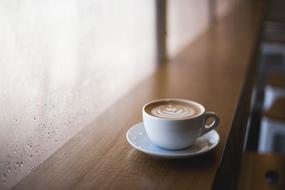 Coffee in a small cup on the wooden surface with the rain outside