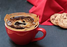 Beautiful, red cup of coffee near the red fabric and cookies