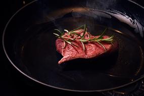 meat with rosemary in a black pan