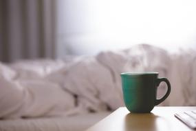 green cup with hot drink on the bedside table