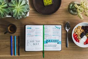 open notebook and Pens on table with coffee and plants