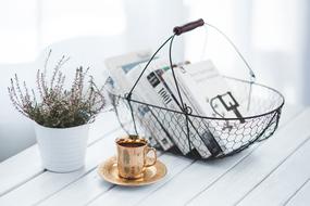 cup of coffee, books in a basket and a pot plant on the table