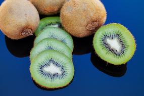 Close-up of the beautiful, colorful kiwi fruits, with the slices, with the reflections on the blue surface