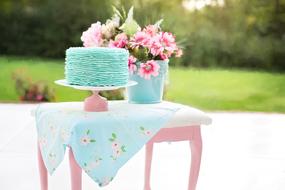 Blue birthday cake and colorful flowers on the table with green blurred background