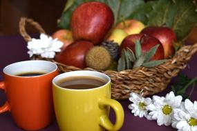 a couple of cups with a drink near a wicker basket with apples