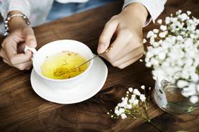 Person, drinking yellow beverage in the white cup, near the beautiful, white flowers