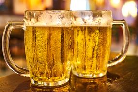 two glass mugs with cold Beer on table on blurred background