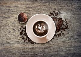 Beautiful cup of coffee, with the beautiful drawing, among the beans, near the chocolate cupcake