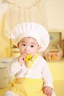 cute asian Baby in chef hat eats bell pepper in Kitchen