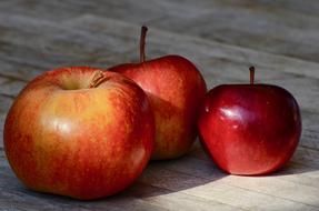 three ripe apples on the table on a wooden surface close up