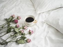 roses and a cup of coffee on a white bed