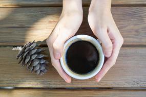 a cup of coffee in hand and a pine cone