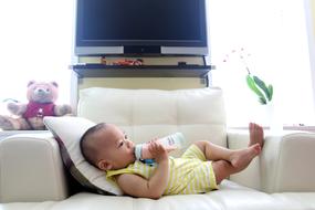 baby drinks milk from a bottle lying on a white armchair