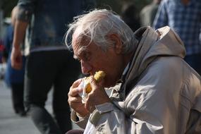 elderly man is eating boiled corn outdoors