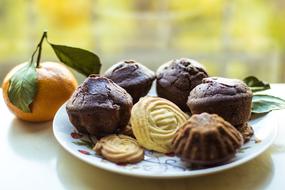 chocolate muffins and cookies on a plate and mandarin on the table