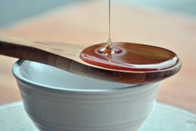 Honey pouring in wooden spoon on blue bowl