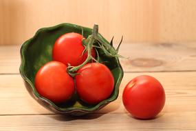 Red tomatoes on the green branch on the wooden surface