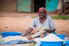 African woman sits on ground making food