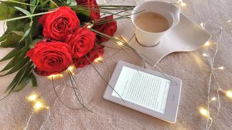 a bouquet of red roses a cup of coffee with milk and an e-book on the table