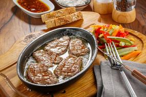 steak in a pan, sliced colored vegetables and bread on a table in a restaurant