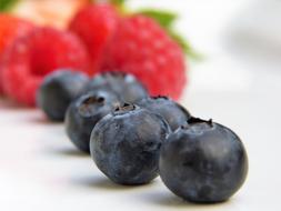 ripe raspberries and blueberries on a white table