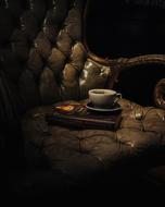 cup of coffee and a book on a leather chair In the dark