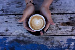 girl's hands on a black cup with cappuccino