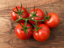 red tomatoes on a branch on a wooden table