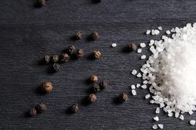 Close-up of the beautiful and colorful pepper balls and white salt on the wooden table