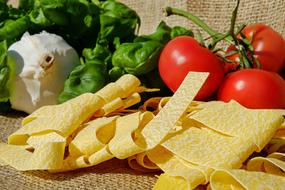 Beautiful, raw Tagliatelle pasta, near the red, shiny tomatoes, basil and garlic