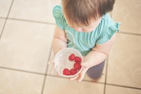 Toddler girl holding bowl with Raspberries