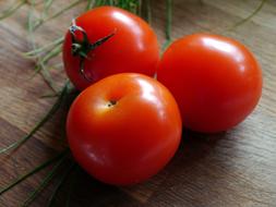 three red ripe tomatoes on a wooden surface close up