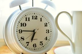 white alarm clock and coffee cup