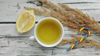 Yellow tea in the cup, lemon, colorful and beautiful candy and plants on the wooden surface