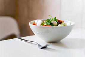 Colorful and beautiful salad in white bowl, and fork, on the white table