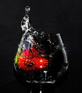 Close-up of the beautiful, shiny glass, with the beautiful, red strawberries in the water, at black background