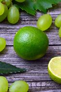 Beautiful green limes, grapes and leaves on the wooden surface