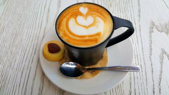 Cup of coffee, with the beautiful drawing, on the saucer, with the beautiful cookie and spoon