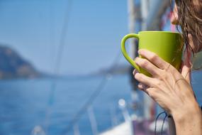 Girl holding a green cup in her hand at blurred background with water