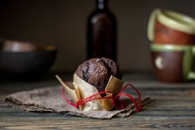 Beautiful, brown brownie muffin in the package with ribbon, near the bottle, bowls and cups, on the wooden table